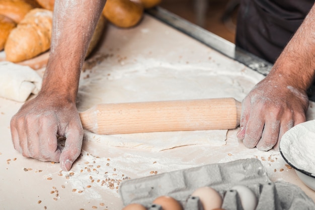 La mano del panadero masculino que aplana la pasta con el rodillo