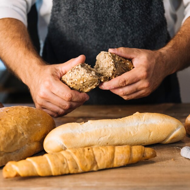 Mano de panadero rompiendo pan de grano entero sobre el escritorio de madera