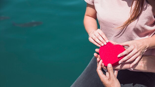 Mano de la pareja con forma de corazón rojo cerca del mar