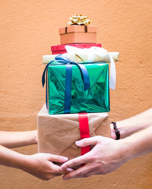 La mano de la pareja sostiene la pila de regalos sobre fondo naranja