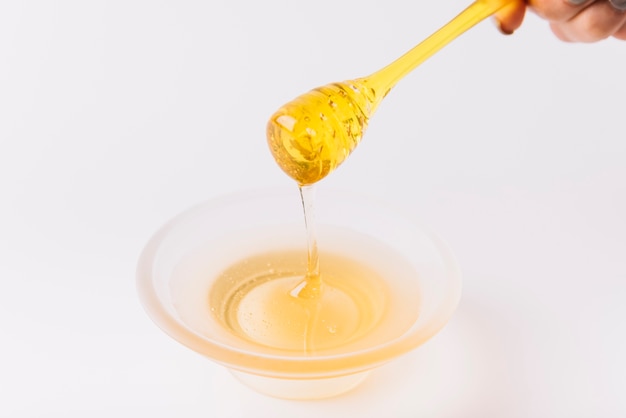 La mano de un perón sosteniendo el cazo sobre el cuenco de miel.