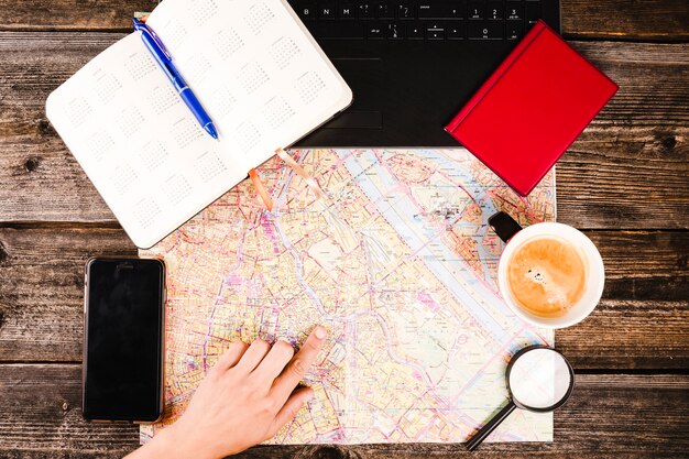 Mano de la persona apuntando a la ubicación en el mapa con café y teléfono inteligente en la mesa