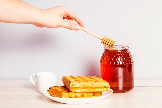 La mano de la persona con cucharón recogiendo miel del frasco para el desayuno