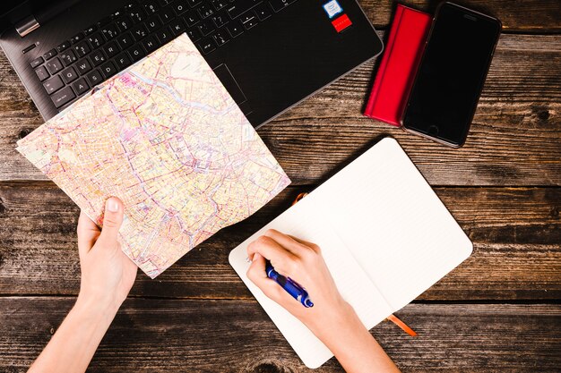 La mano de una persona escribiendo en el bloc de notas mientras sostiene el mapa sobre la mesa