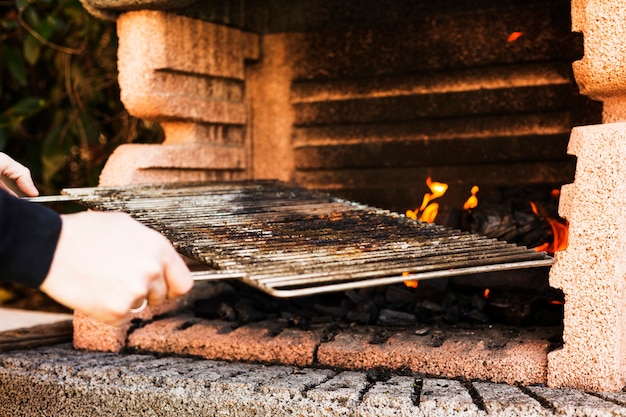 Mano de una persona que sostiene la hoja de metal de la barbacoa al aire libre