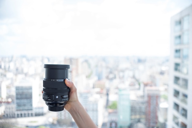 Foto gratuita la mano de la persona que sostiene la lente de la cámara delante de fondo de edificios borrosos