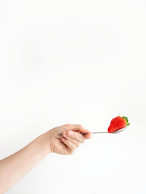 Mano de la persona sosteniendo una cuchara con una fresa sobre una superficie blanca
