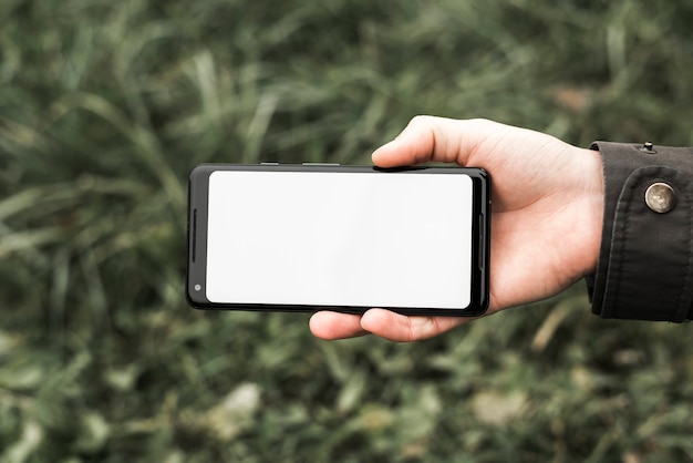 La mano de una persona sosteniendo un teléfono móvil que muestra una pantalla blanca en blanco al aire libre