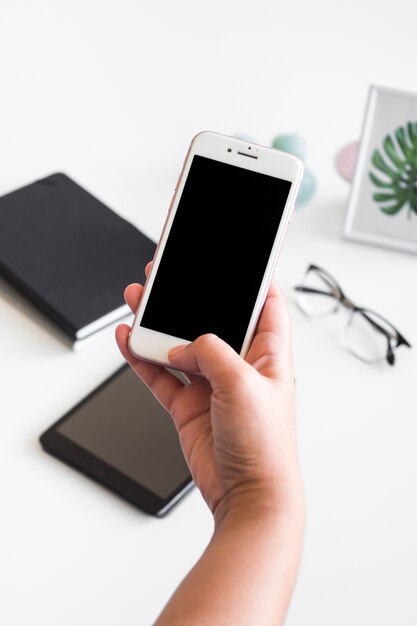 Mano de la persona con el teléfono inteligente cerca de la mesa con anteojos y tableta