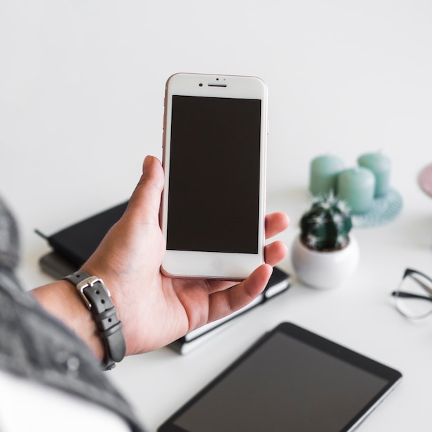 Mano de la persona con teléfono inteligente cerca de la mesa con equipos