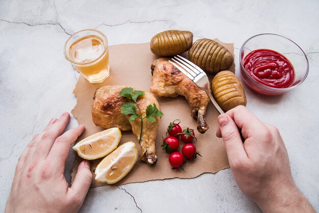 Mano de persona con tenedor contra pollo asado con papas y cerveza