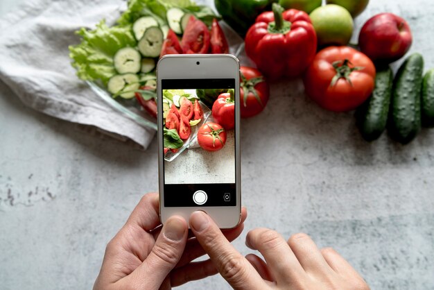 Una mano de persona tomando foto de vegetales frescos en el fondo