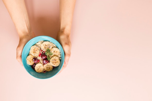 Mano plana laico sosteniendo tazón de avena y frutas con espacio de copia