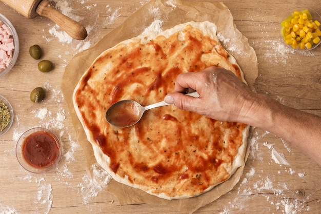 Mano plana pone la salsa de tomate para untar sobre la masa de pizza