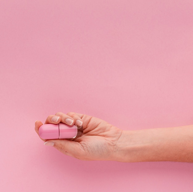 Mano de primer plano sosteniendo esmalte de uñas rosa