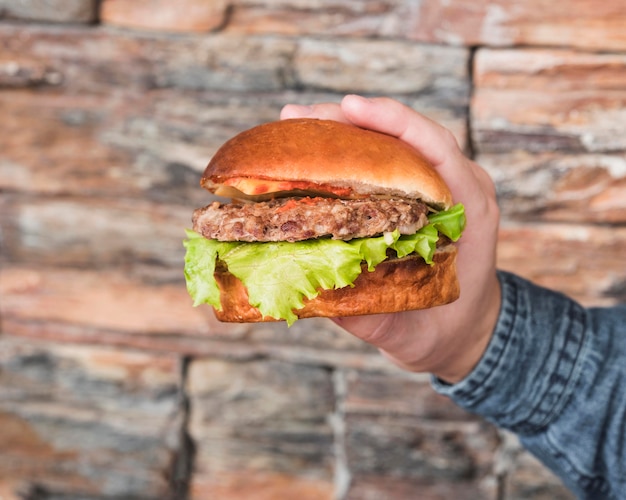 Mano de primer plano sosteniendo sabrosa hamburguesa