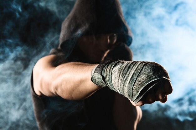 Mano de primer plano con vendaje de kickboxing de entrenamiento de hombre musculoso en humo negro y azul