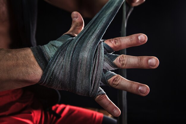 Mano de primer plano con vendaje de kickboxing de entrenamiento de hombre musculoso en negro