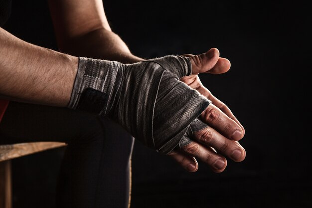 Mano de primer plano con vendaje de kickboxing de entrenamiento de hombre musculoso en negro