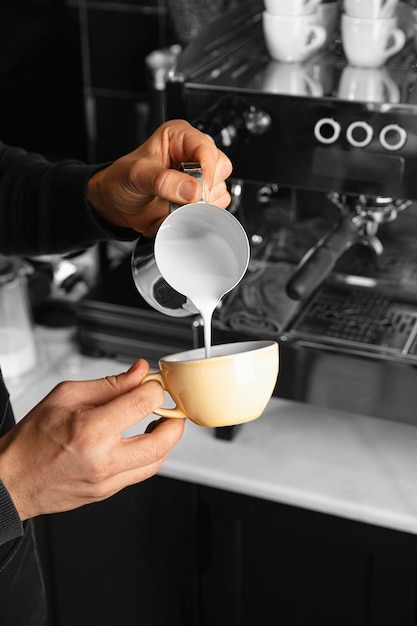 Mano de primer plano vertiendo leche en taza