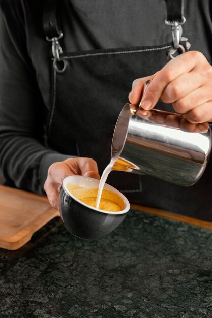 Mano de primer plano vertiendo leche en taza