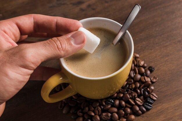 Mano que sostiene el azúcar cerca de la taza con café