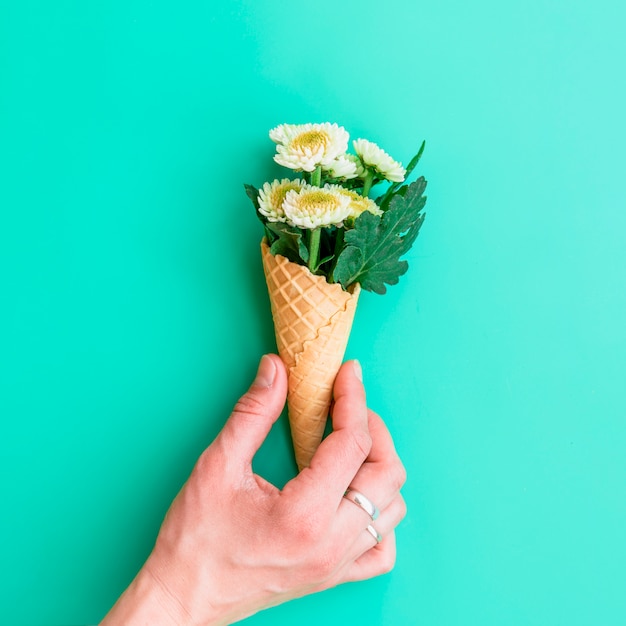 Mano que sostiene el cono de galleta con flores blancas