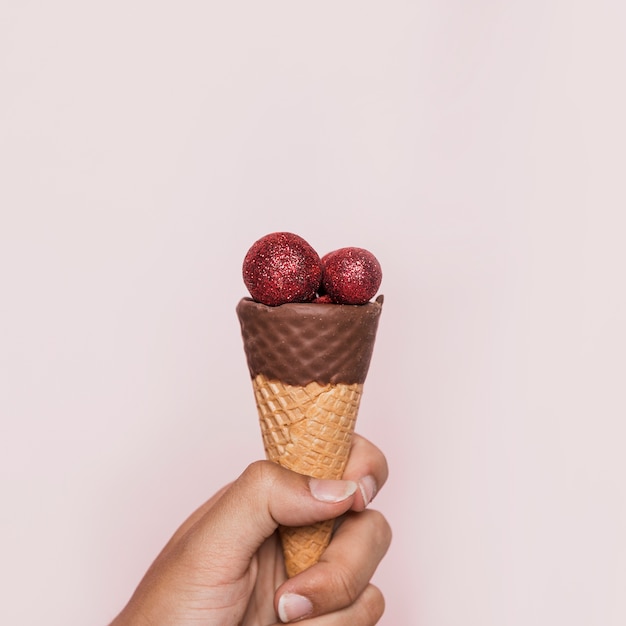 Mano que sostiene el cono de helado con bolas de discoteca rojas