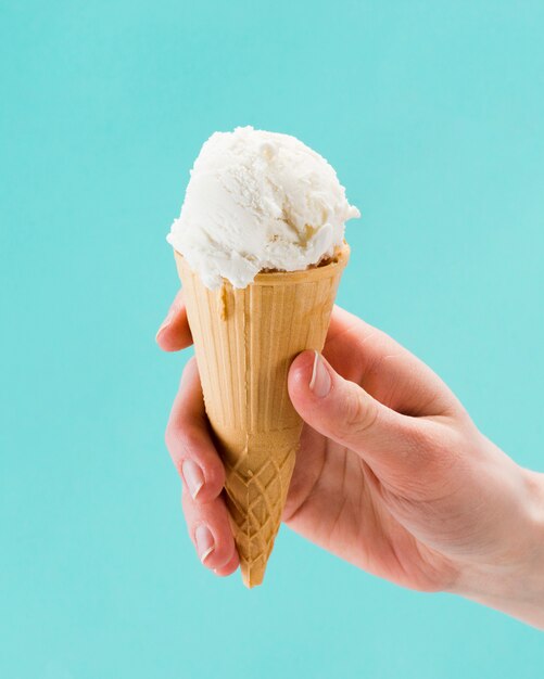 Mano que sostiene el cono de helado de vainilla sobre fondo azul