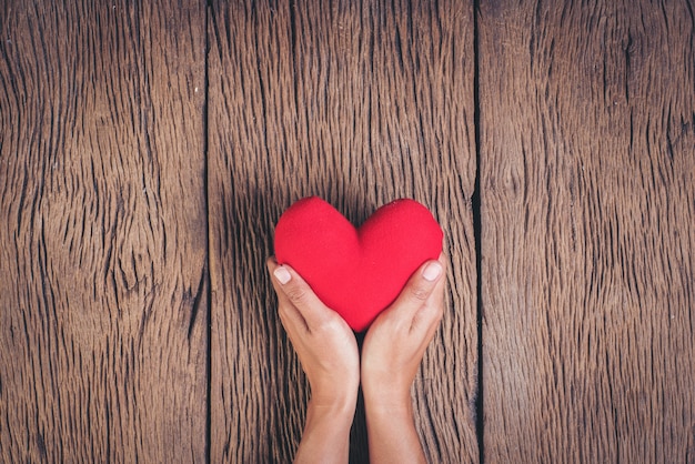 Mano que sostiene el corazón rojo sobre fondo de madera