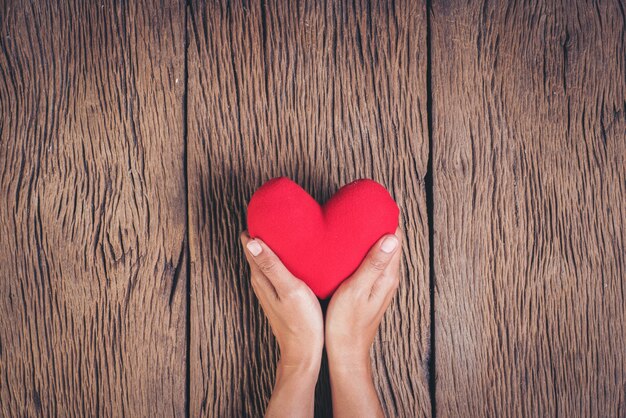 Mano que sostiene el corazón rojo sobre fondo de madera