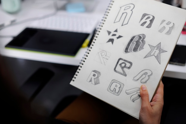 Mano que sostiene el cuaderno con Drew Brand Logo Ideas de diseño creativo