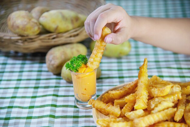 Mano que sostiene la deliciosa papa frita en un plato de madera con salsa bañada