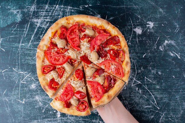 Mano que sostiene la deliciosa pizza de pollo con tomates en mármol.