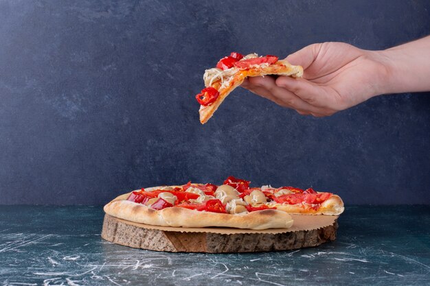 Mano que sostiene la deliciosa pizza de pollo con tomates en mármol.