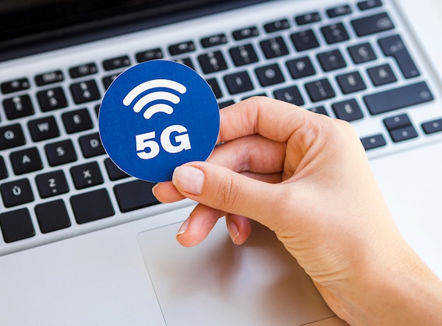 Mano que sostiene la etiqueta 5g por encima del portátil