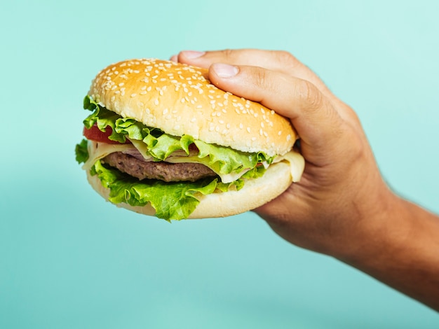 Mano que sostiene la hamburguesa deliciosa con fondo azul