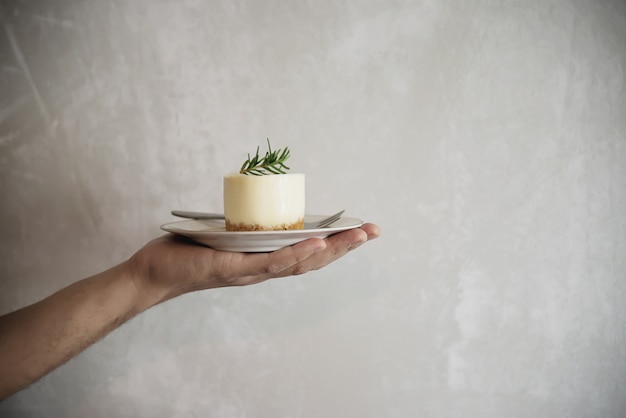 Mano que sostiene el postre sobre fondo de pared de cemento de bandeja