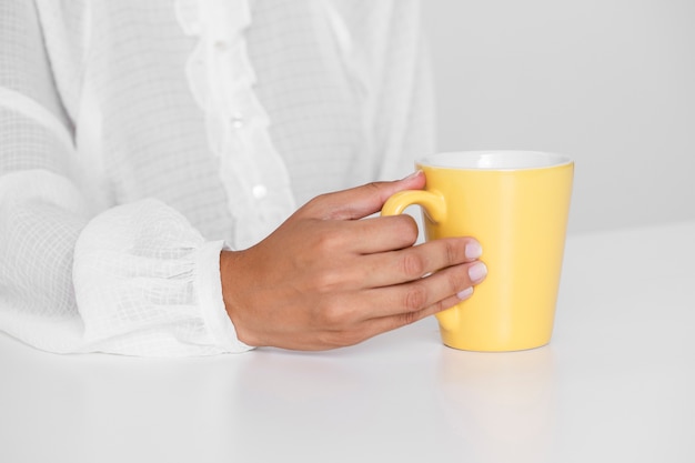 Foto gratuita mano que sostiene la taza amarilla sobre una mesa