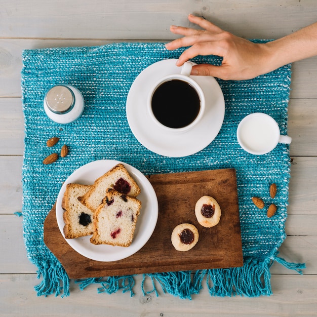 Mano que sostiene la taza de café cerca de la placa con pastel