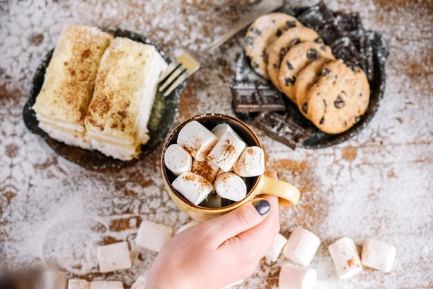 Mano que sostiene la taza en la mesa con dulces