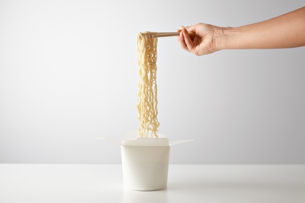 Foto gratuita la mano recoge sabrosos fideos hervidos de la caja de papel en blanco para llevar wok abierto aislado en blanco en el centro