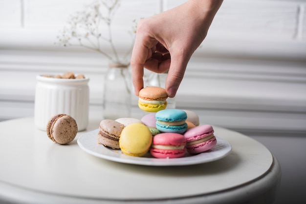 Foto gratuita mano recogiendo el macarrón de un plato blanco mantenido en la mesa blanca