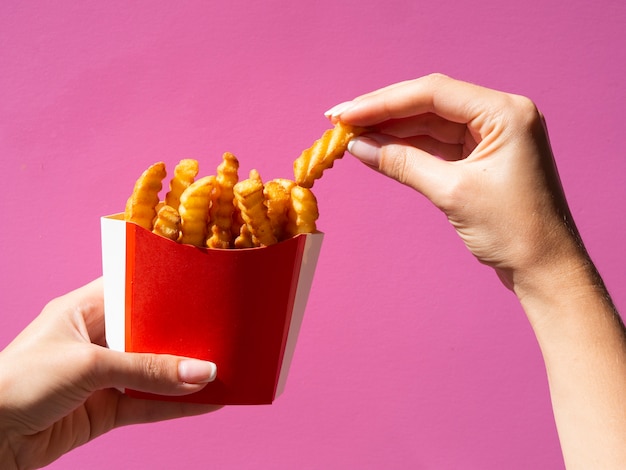 Foto gratuita mano recogiendo papas fritas sobre fondo rosa