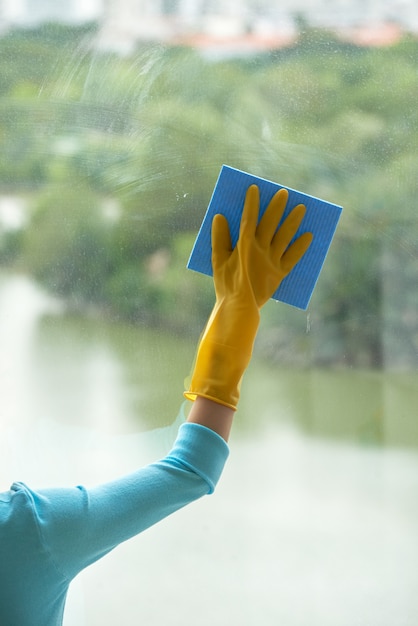 Mano recortada de mujer irreconocible limpiando ventana panorámica