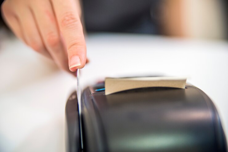 Mano roba crédito rojo a través de terminal de pago. Tarjeta de débito en la terminal. Máquina de lector de tarjetas de crédito sobre fondo blanco
