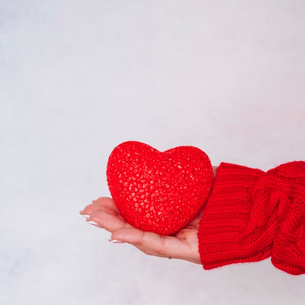 Mano de señora en suéter con corazón decorativo.