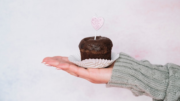 Mano de señora en suéter con muffin de chocolate con vela.