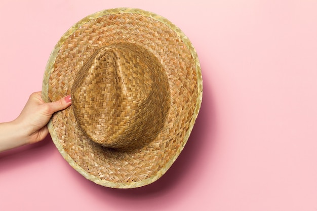 Mano de sombrero de paja del verano de la explotación agrícola de la mujer joven en fondo rosado. Fondo De La Moda. Concepto Del Verano.