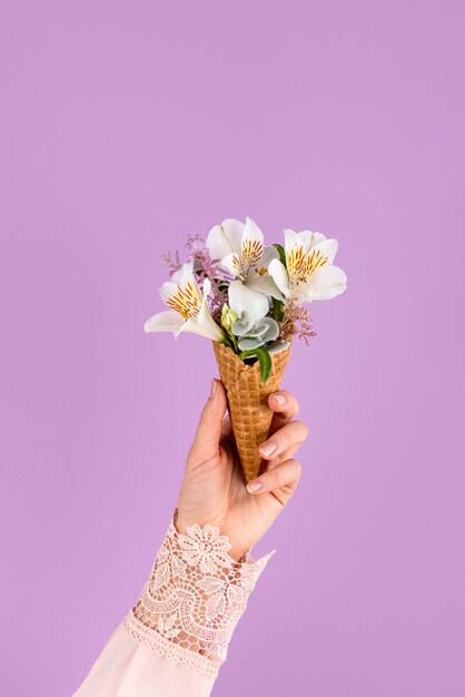 Mano sosteniendo cono de helado con flores